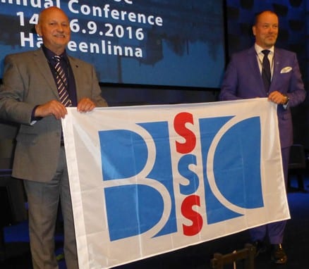 Bilde av Roger Ryberg og Ossi Savolainen som holder en fane av logoen til BSSSC