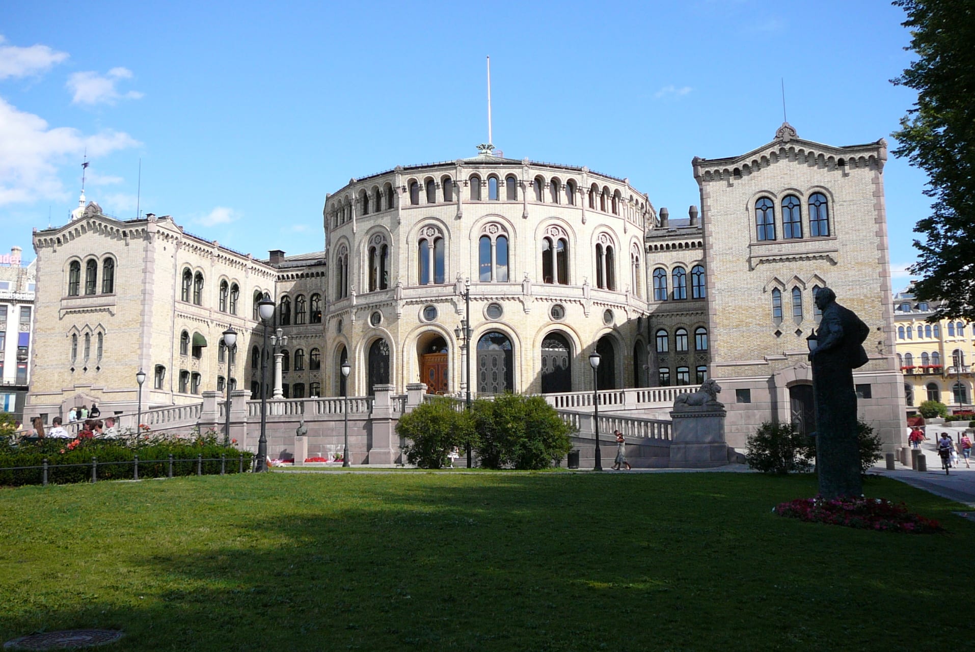 Bilde av Stortinget en sommerdag med grønt gress i forkant og blå himmel i bakgrunnen.