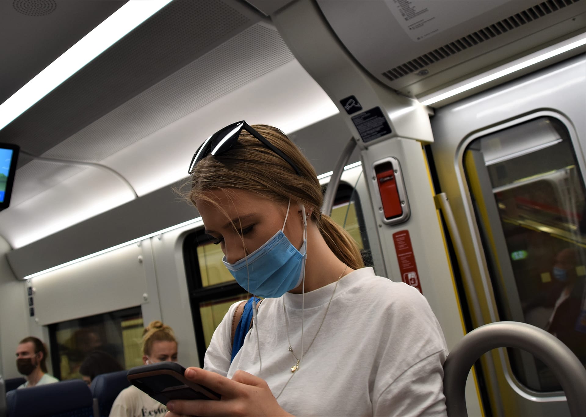 Bilde av en kvinne med mobiltelefon på t-bane med munnbinn på,