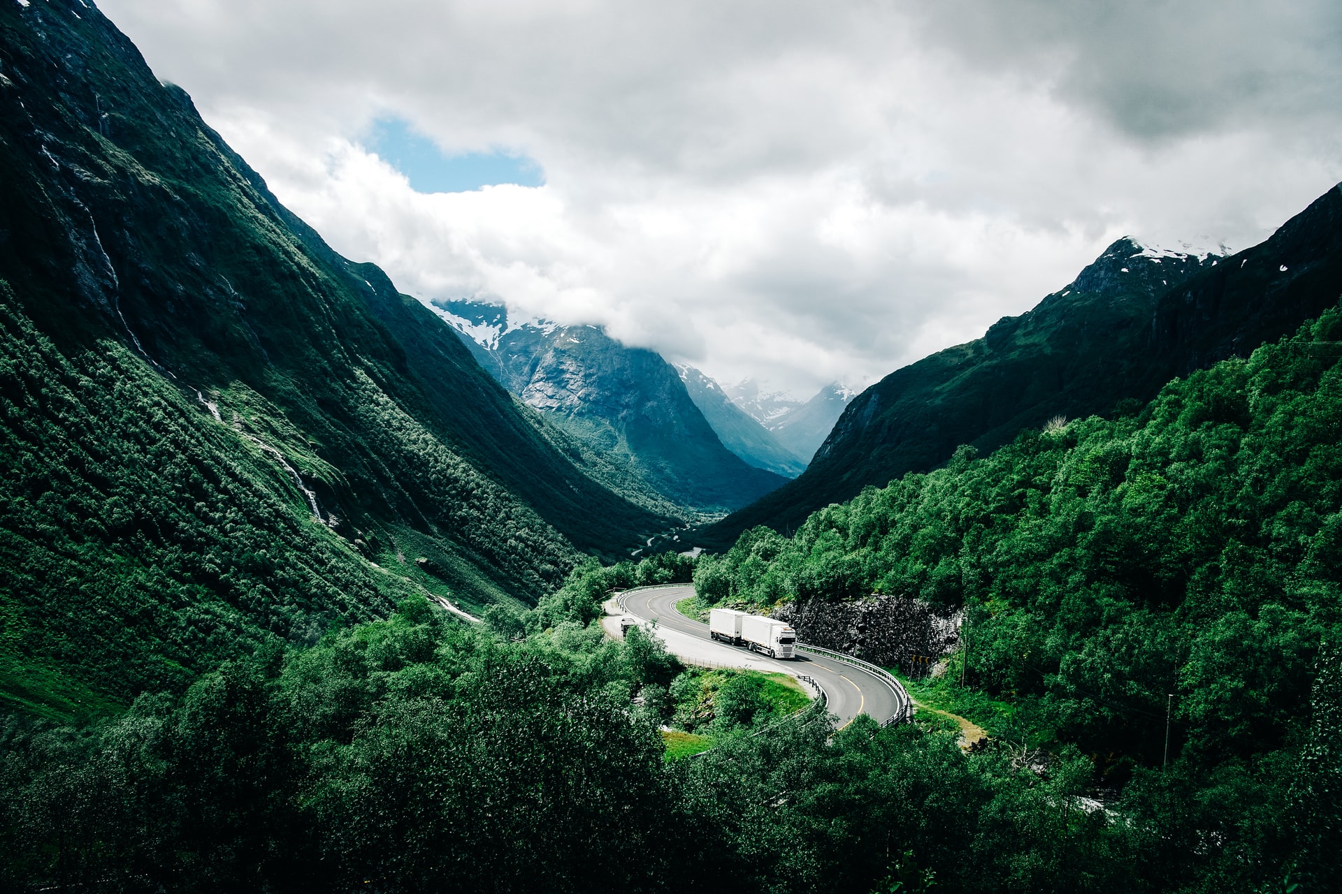 Lastebil som kjører gjennom et skogkledd landskap med fjell i bakgrunnen.