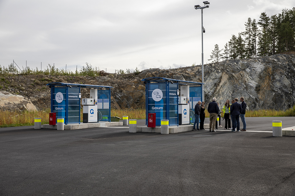 To biogassfyllestasjoner på Innlandsporten i Stange kommune. Åtte personer står i ring ved den ene og har en samtale.